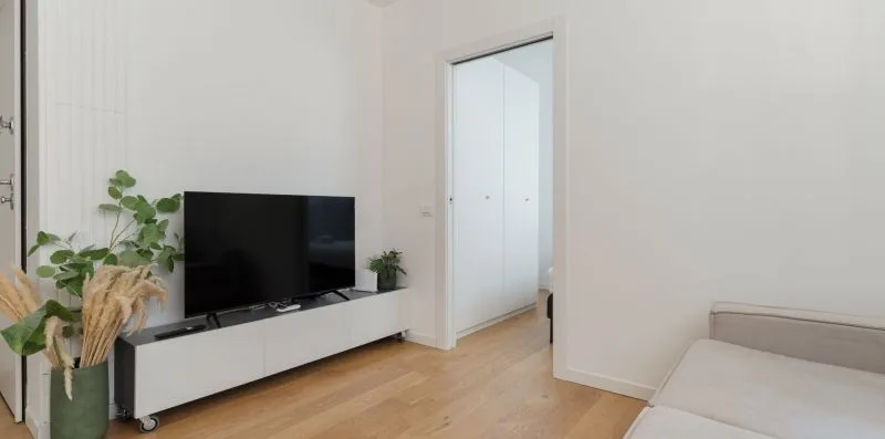 Una sala luminosa con un televisor sobre un mueble bajo y asientos de color claro.