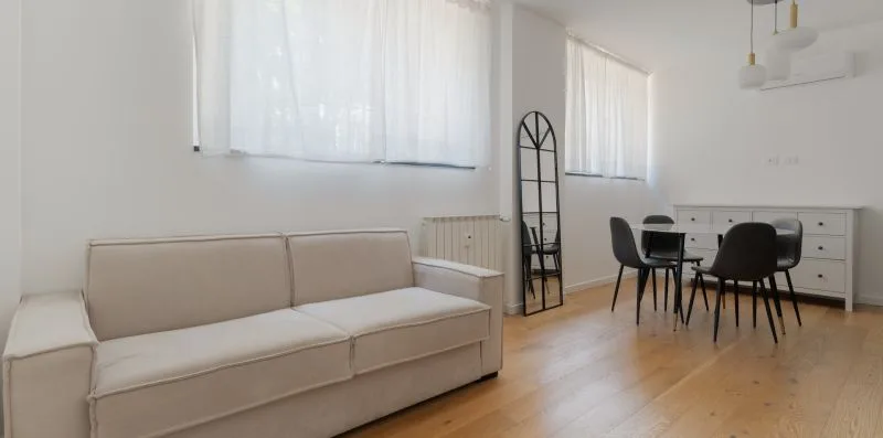 Una luminosa sala de estar y comedor con asientos, una mesa y ventanas grandes.