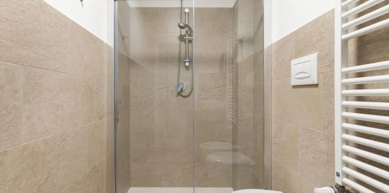 Un baño alicatado con ducha de pared y radiador toallero blanco.