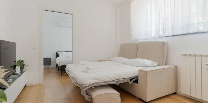 Un dormitorio luminoso con una cama junto a una ventana grande con cortinas translúcidas.