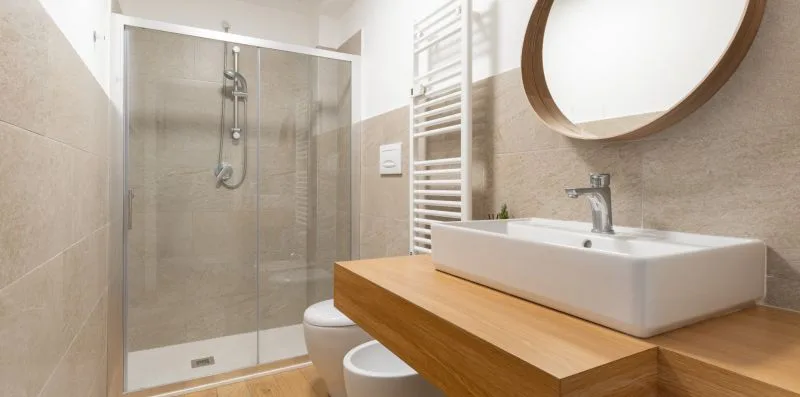 Un baño con ducha de vidrio, lavabo y espejo redondo en la pared.