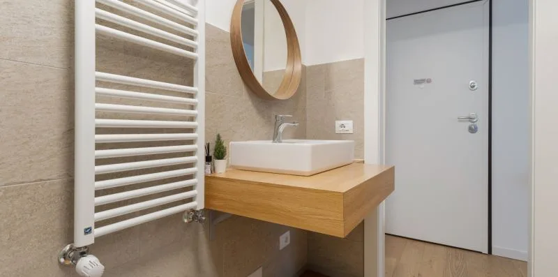 Un baño con un mueble de madera, espejo de pared y toallero calefactor.