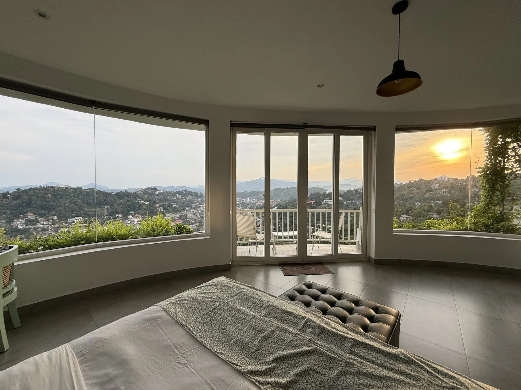 Dormitorio con ventanas curvas en la esquina que enmarcan las colinas de Kandy