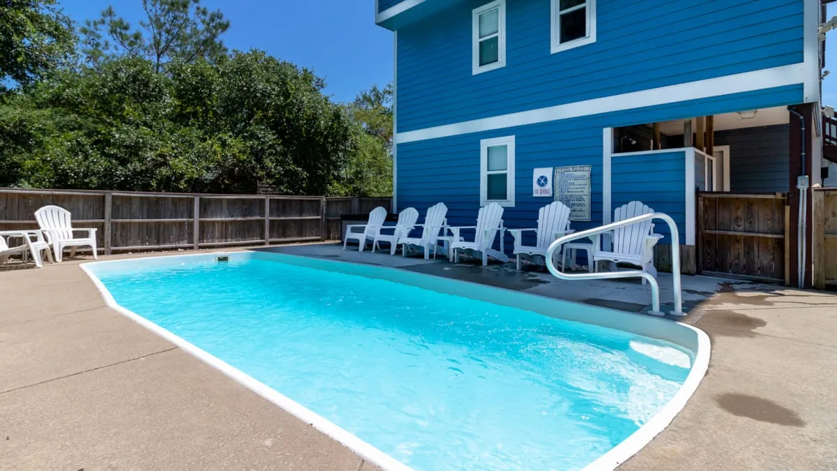 An outdoor swimming pool beside a blue building, with seating along the deck.