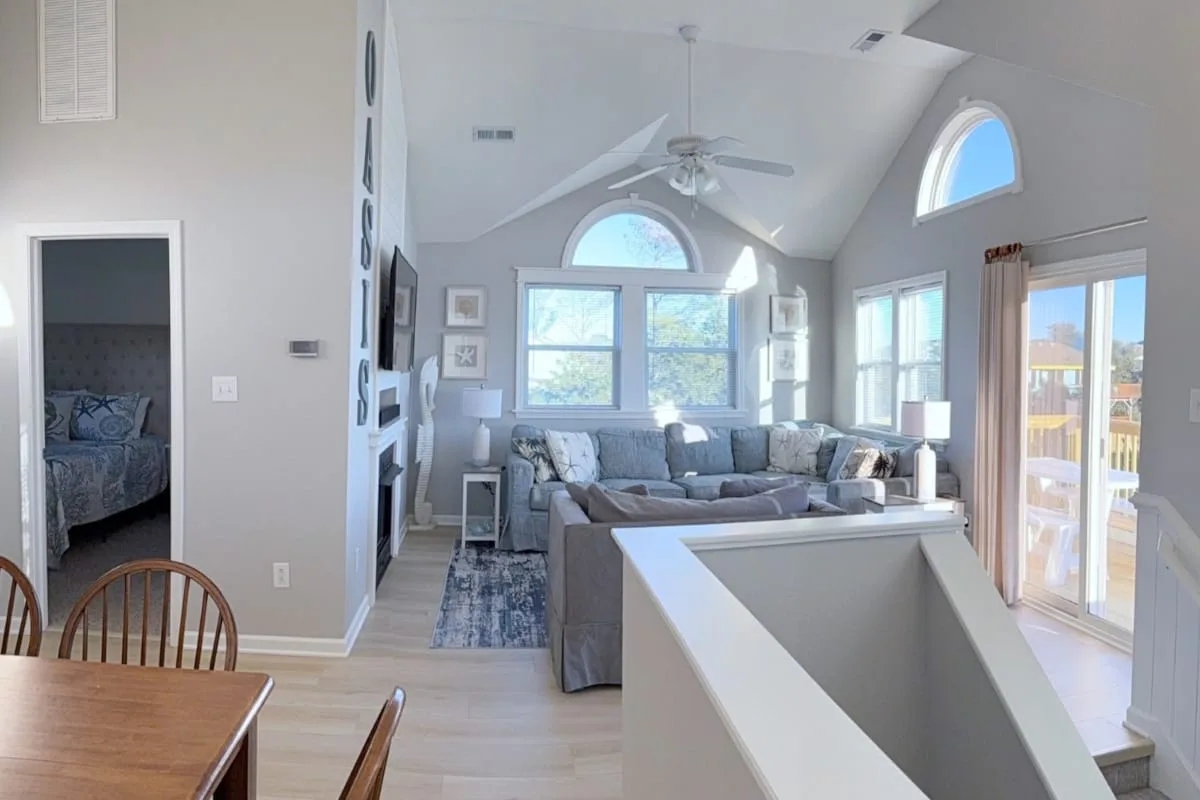 A bright living room with a sectional sofa, large windows, and a vaulted ceiling.