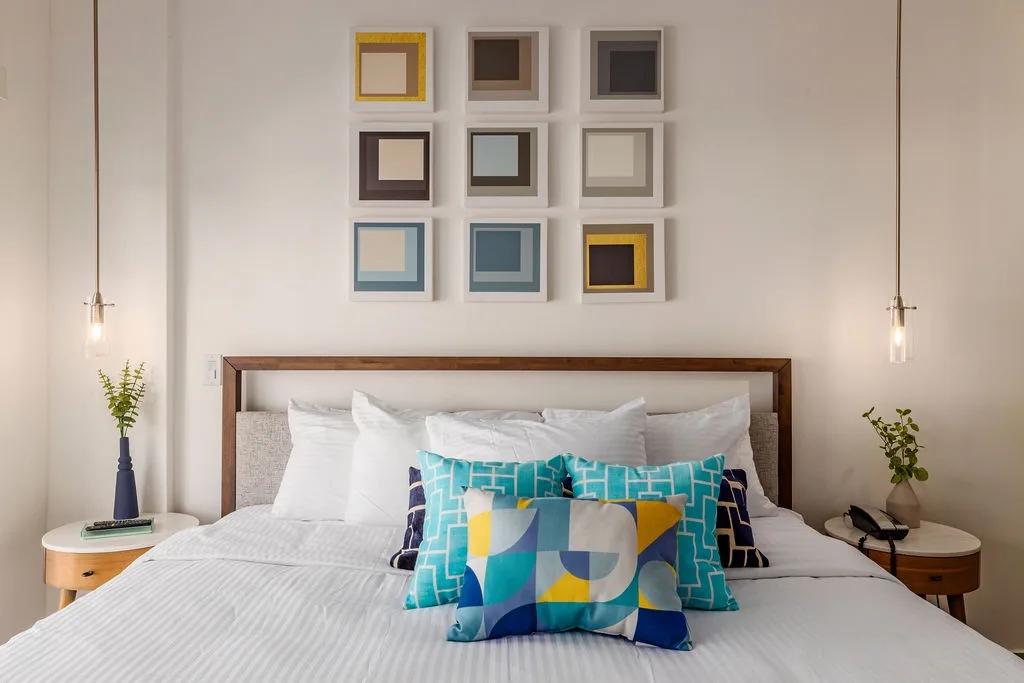 Sink into crisp white linens and plush pillows in your modern bedroom, where vibrant artwork and warm pendant lighting create a welcoming retreat after a day of exploring.