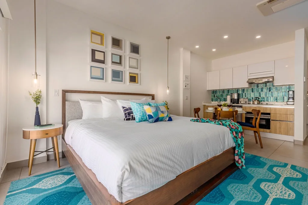 Your bright studio features crisp white linens and playful turquoise accents, with a modern kitchenette just steps from your cozy bed—perfect for feeling at home.