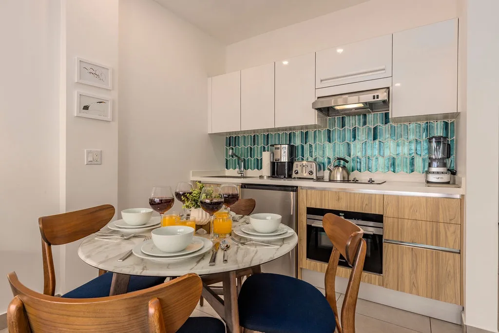 Your modern kitchen features sleek appliances and a stylish teal backsplash, with a cozy marble dining table set for a delightful meal, perfect for intimate mornings or casual evenings together.