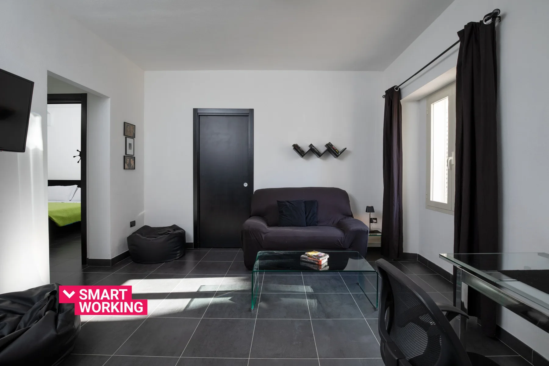 A living room with dark seating, a glass coffee table, and a window.