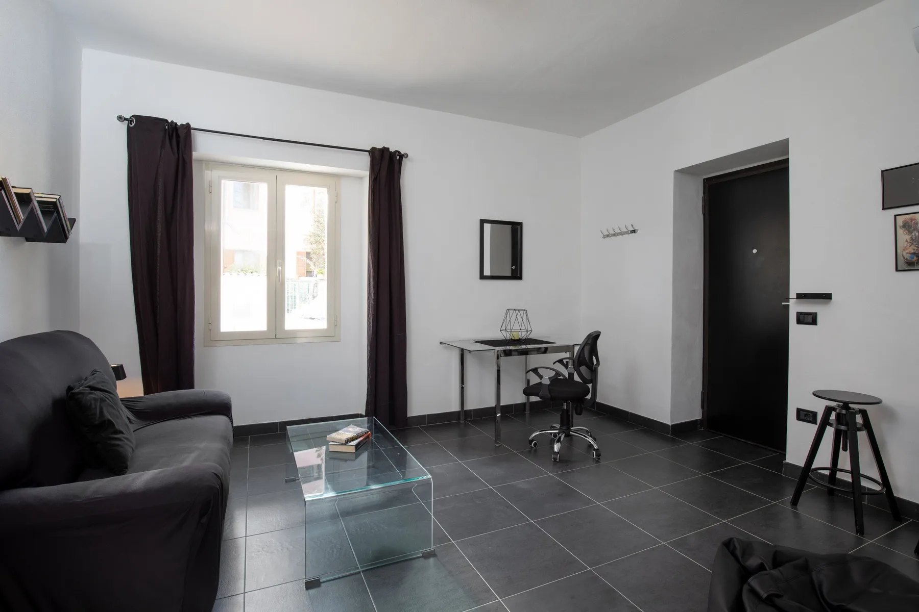 A living area with dark seating, a glass coffee table, and a window.