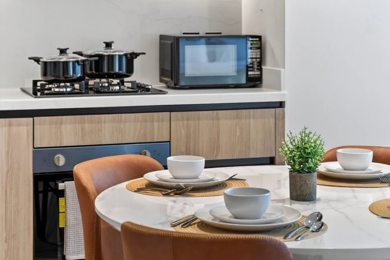 A dining table with place settings sits in front of a kitchen counter and appliances.