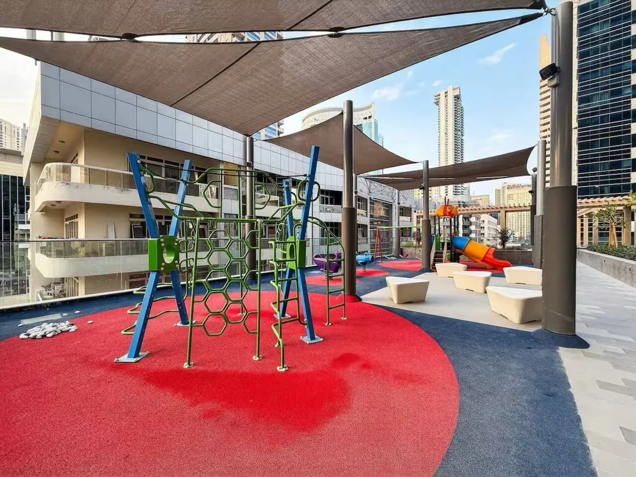 An outdoor playground with climbing equipment sits beneath large shade canopies.