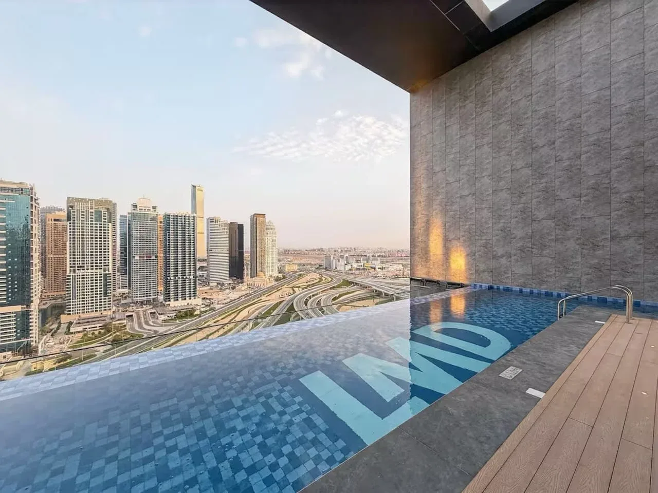 A rooftop pool overlooks a cluster of high-rise buildings and winding roads.