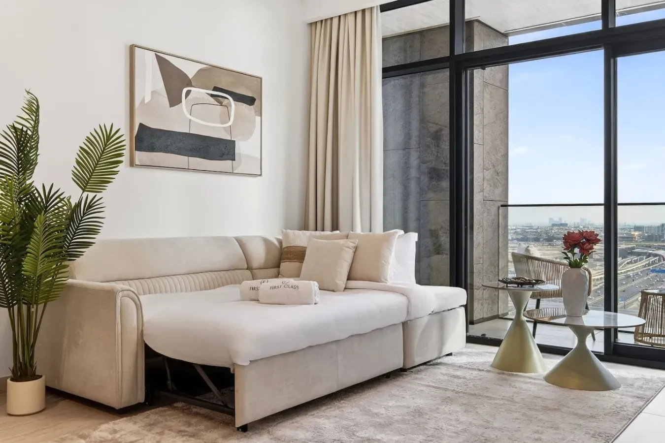 A bright living room with light seating beside large windows overlooking the city.