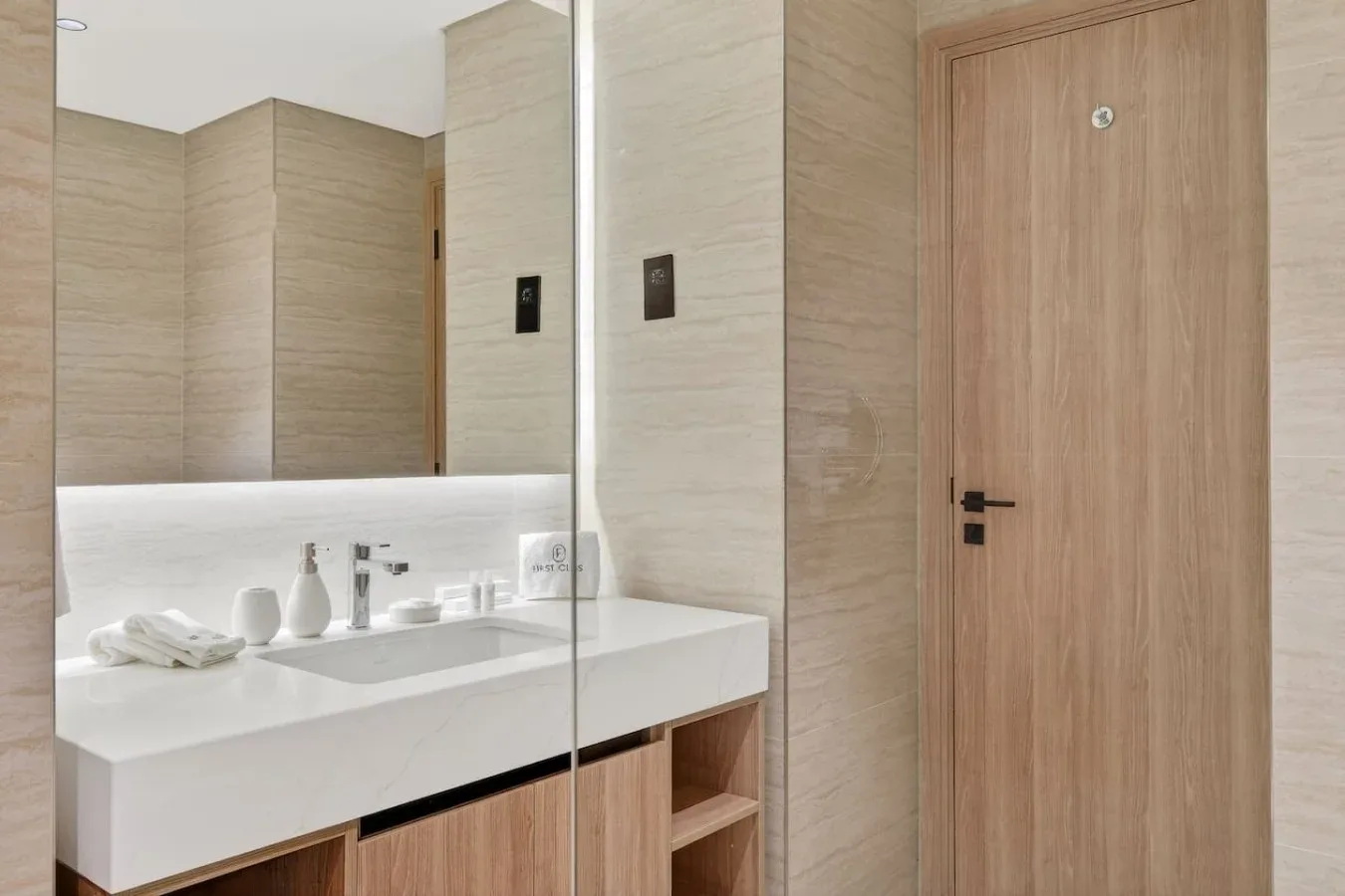 A bright bathroom vanity with a wide mirror and a wooden door.
