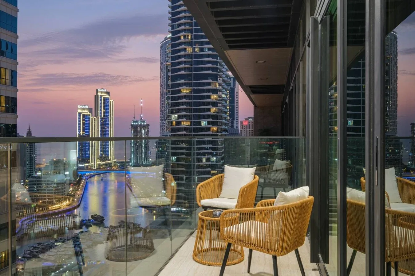A balcony seating area overlooks illuminated city buildings at dusk.