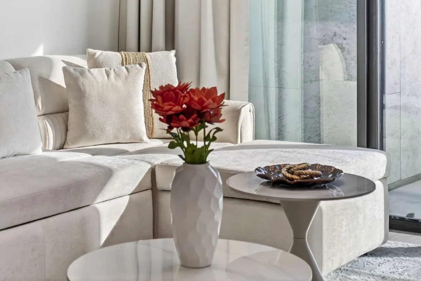 A bright living room with pale seating and flowers on a coffee table.