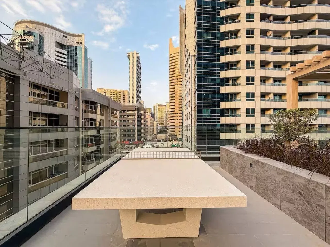 An outdoor terrace with a long table overlooks surrounding city buildings.