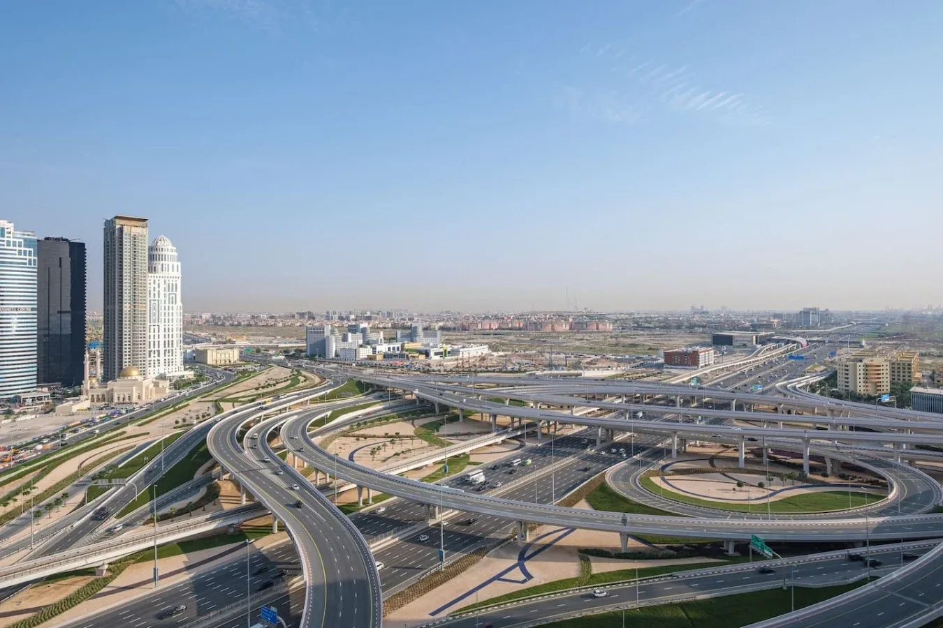 An urban highway interchange curves beneath a clear sky beside several tall buildings.
