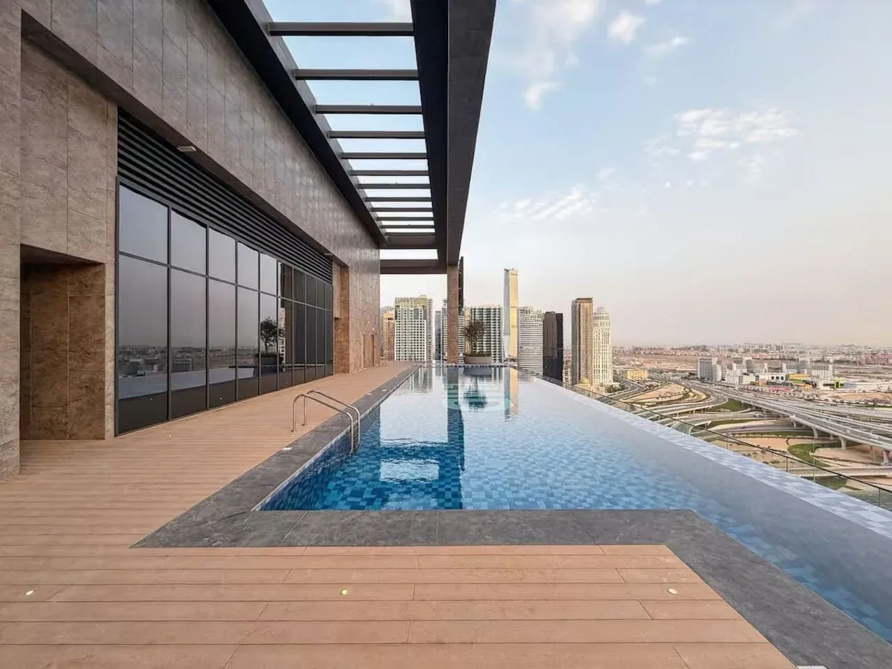 A rooftop swimming pool overlooks nearby buildings beneath an open sky.