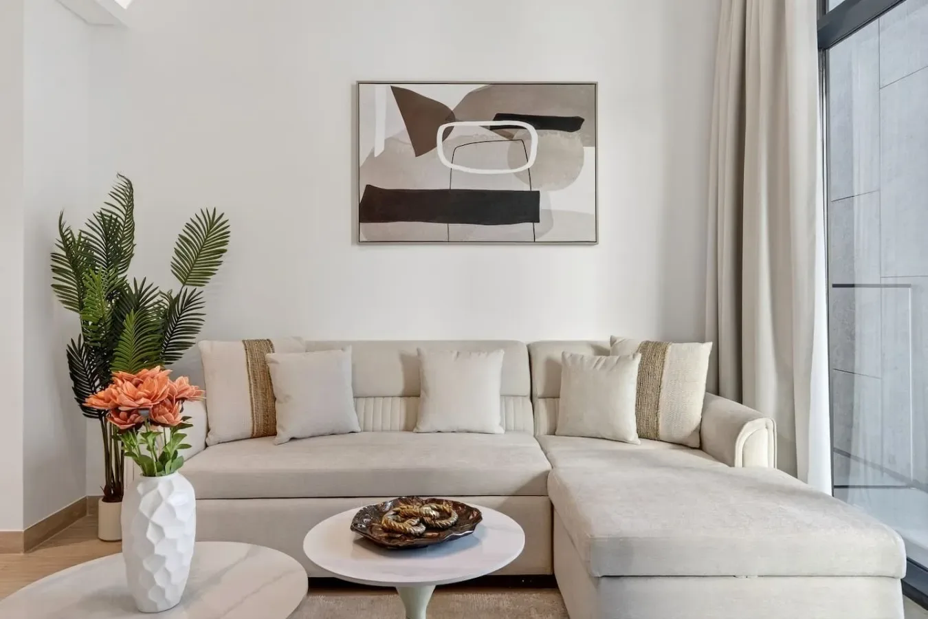 A bright living room with an L-shaped seating area and abstract wall art.