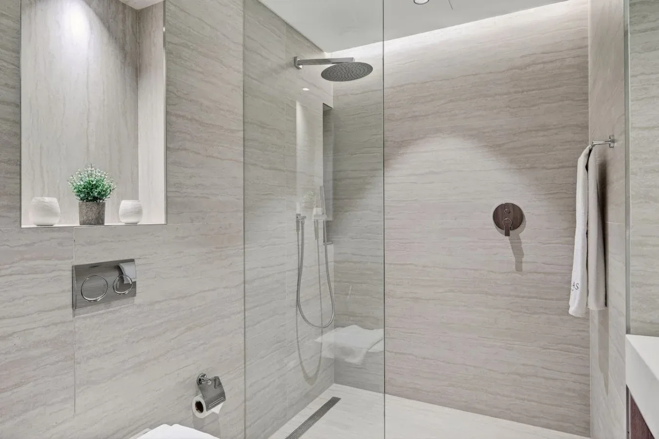 A modern bathroom with a glass shower and light stone walls.