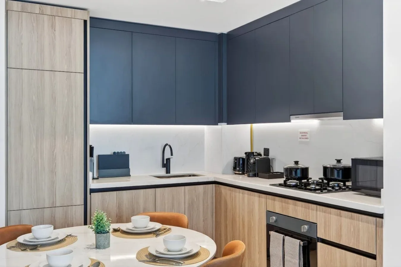 A modern kitchen with dark cabinets, a cooktop, and a round dining table.