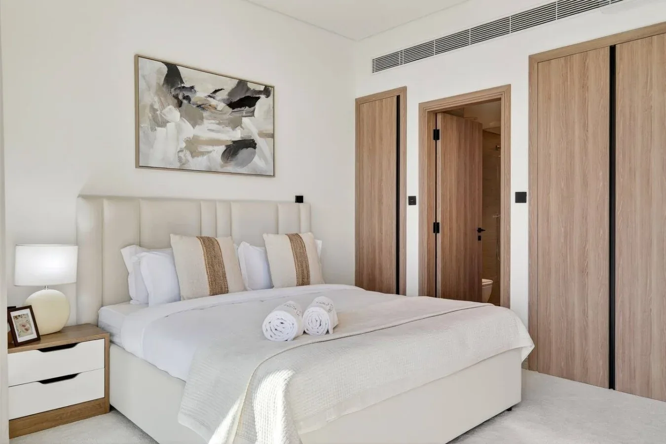 A bright bedroom with a neatly made bed and abstract artwork above the headboard.