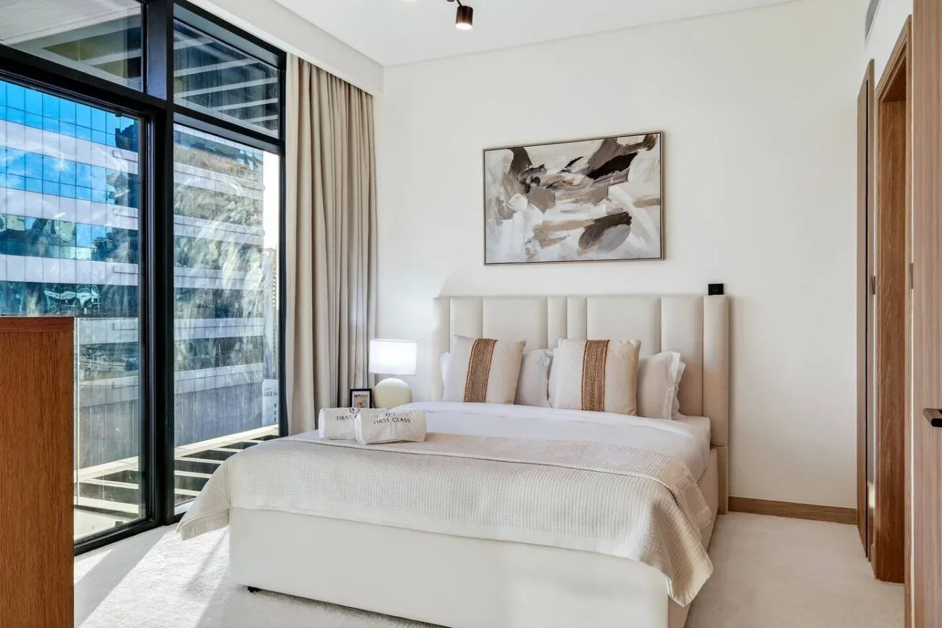 A bright bedroom with a neatly made bed beside large windows.
