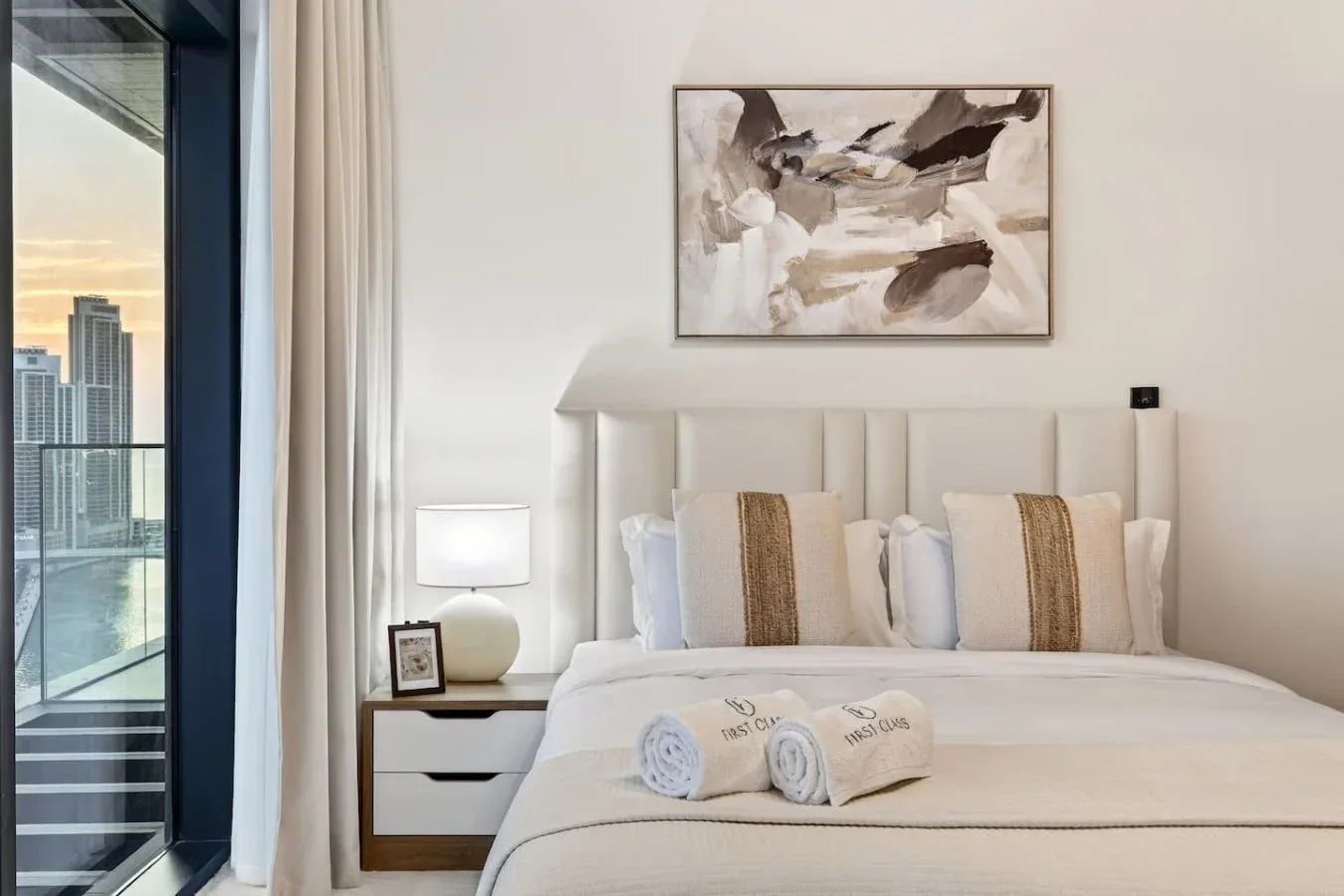 A bright bedroom with a neatly made bed and abstract artwork above the headboard.