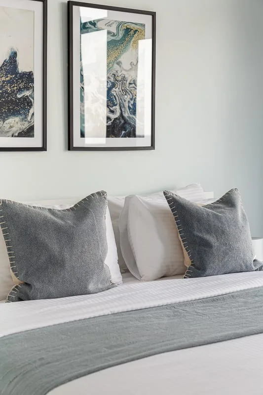 A neatly made bed with gray pillows sits beneath framed artwork.