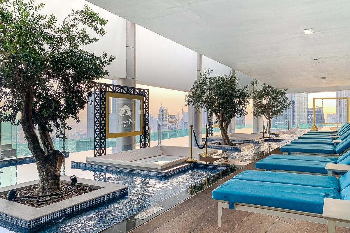A bright indoor poolside lounge has blue cushioned seating beside the water.