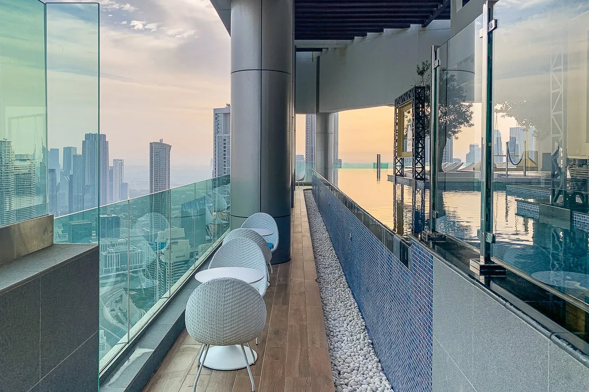 A rooftop pool runs alongside a glass balcony with seating and city views.