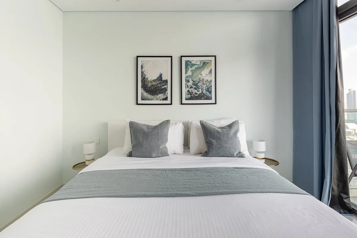 A bedroom with a neatly made bed and framed artwork above it.