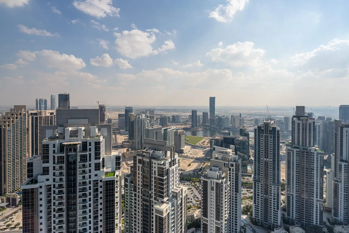 A city skyline with clusters of high-rise buildings beneath a partly cloudy sky.