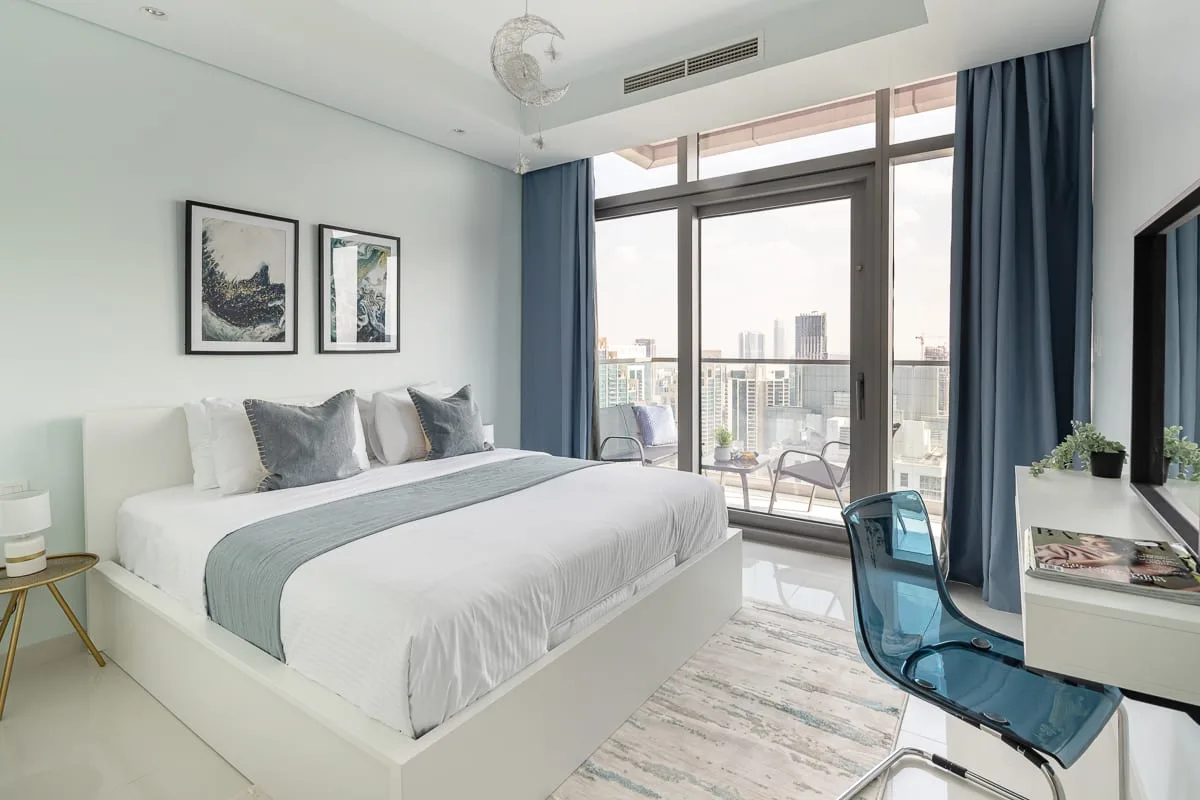 A bright bedroom with a large bed beside windows opening onto a balcony.