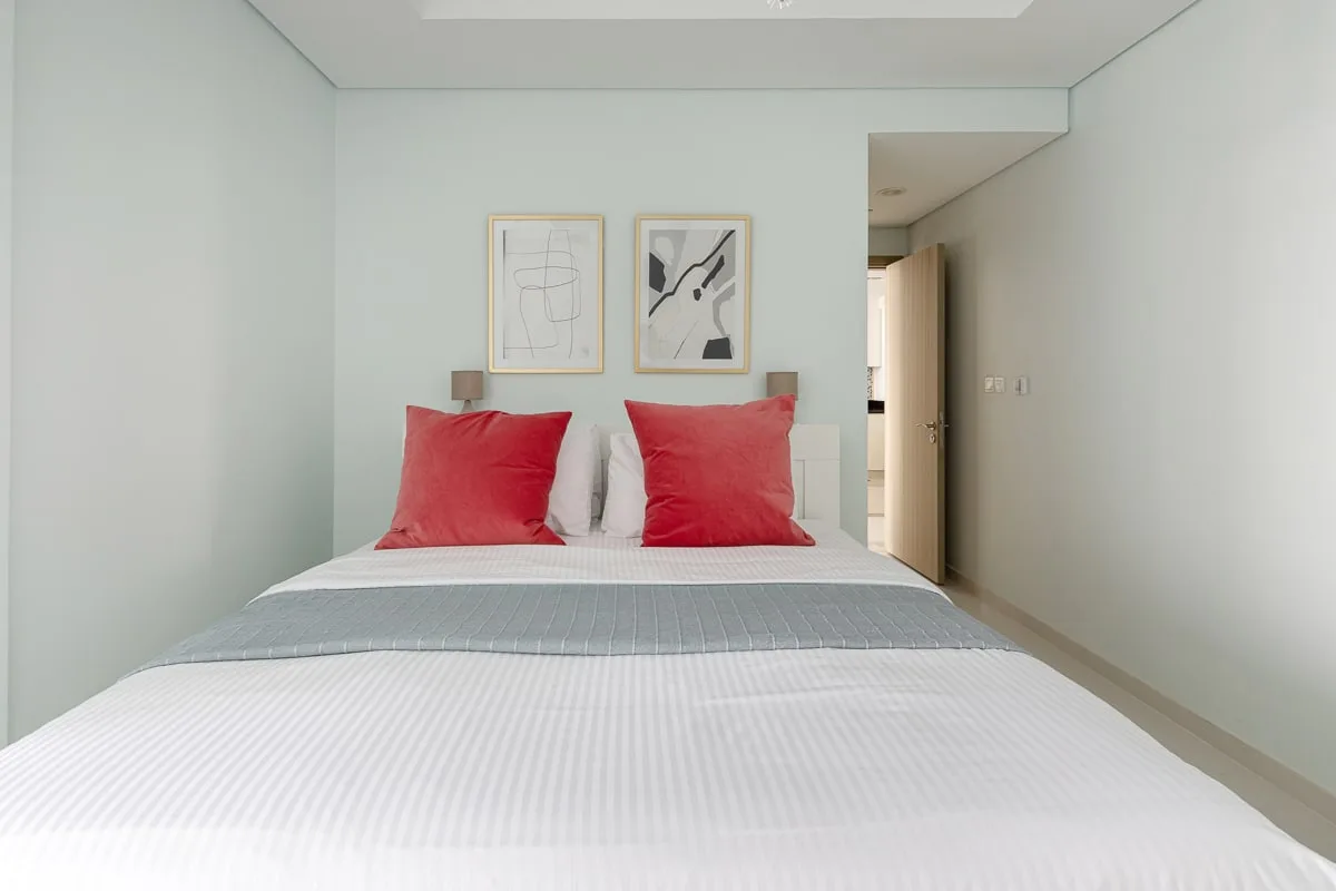 A bedroom with a neatly made bed and red pillows beneath two framed prints.