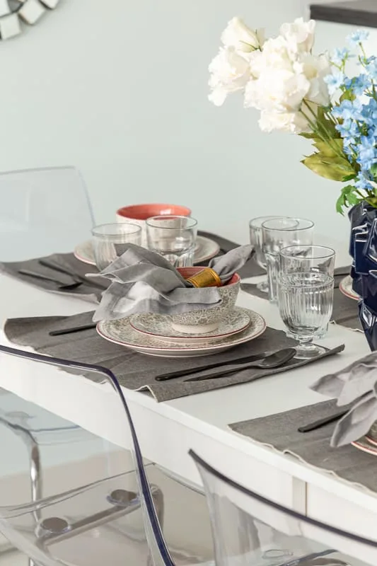 A dining table is set with dishes, glasses, and a flower arrangement.