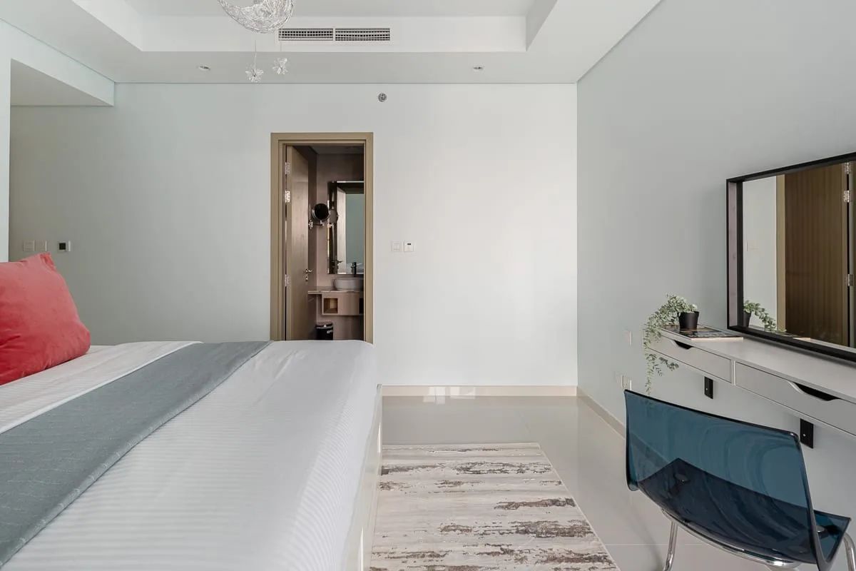 A bright bedroom with a bed, a vanity, and a large mirror.