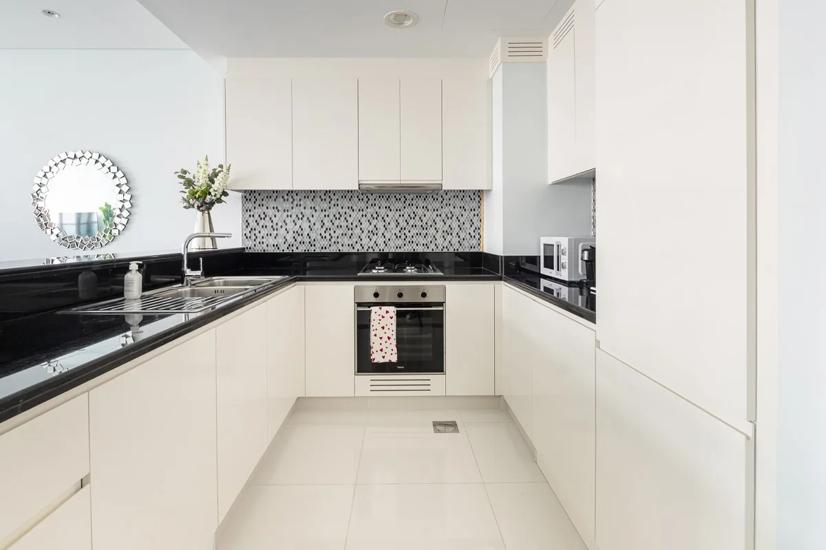 A bright modern kitchen with white cabinets and black countertops.
