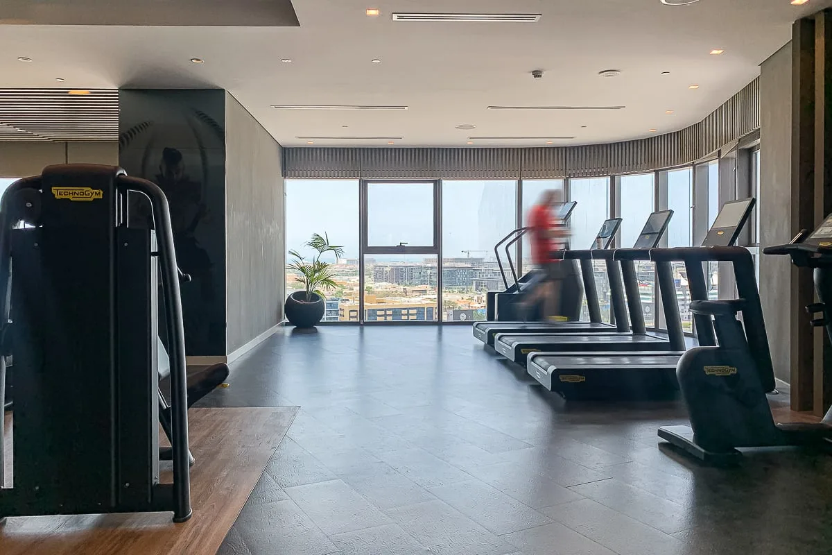 A gym with treadmills arranged beside large windows.