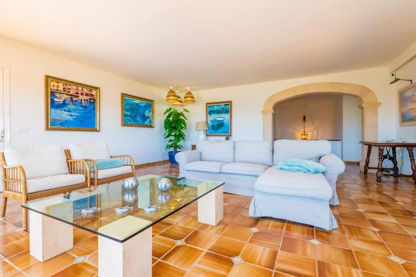 Una sala de estar con asientos claros, una mesa de centro de vidrio y cuadros enmarcados.