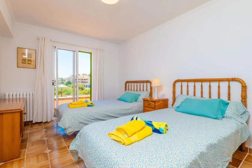 Un dormitorio luminoso con dos camas y una puerta de cristal que da a un balcón.