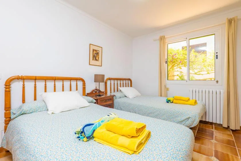 Un dormitorio luminoso con dos camas y una ventana con vista a árboles frondosos.