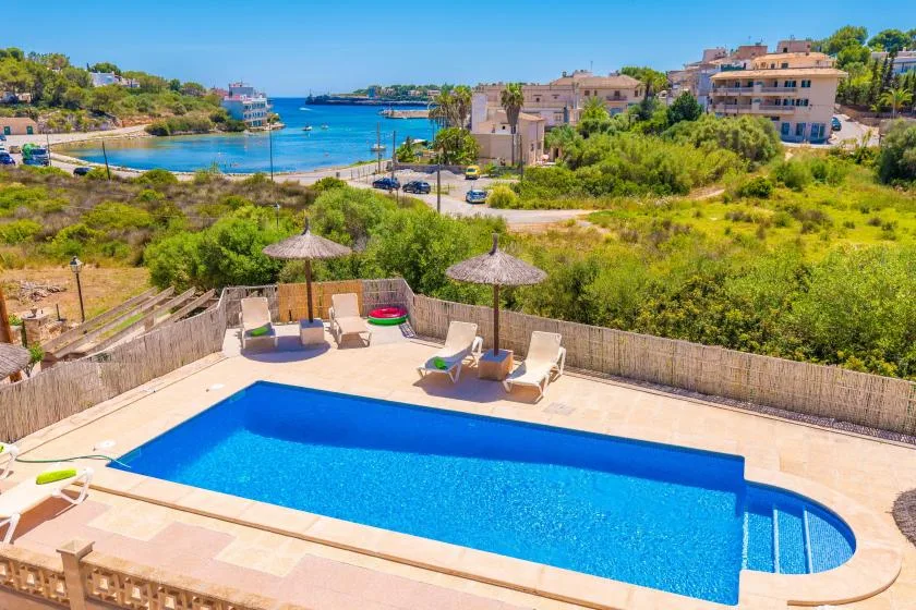 Una piscina al aire libre con tumbonas y sombrillas tiene vistas a una bahía costera.