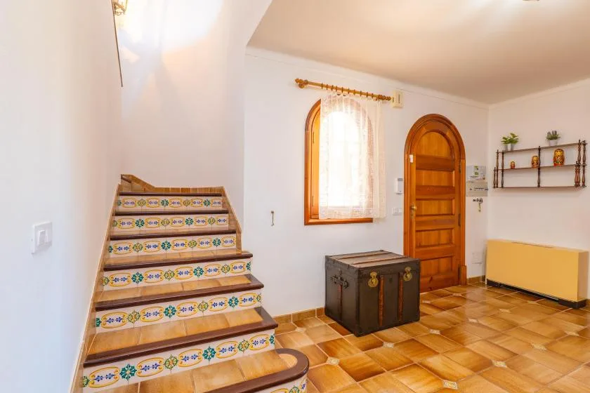 Un interior luminoso con escalones de azulejos, una puerta de madera y una ventana arqueada.