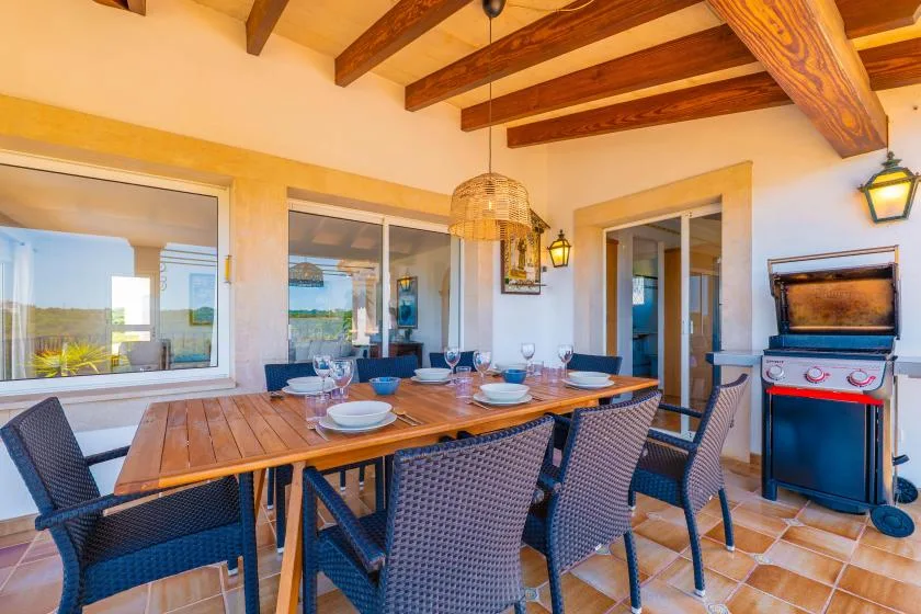 Comedor en un patio cubierto, con una mesa larga y asientos tejidos.