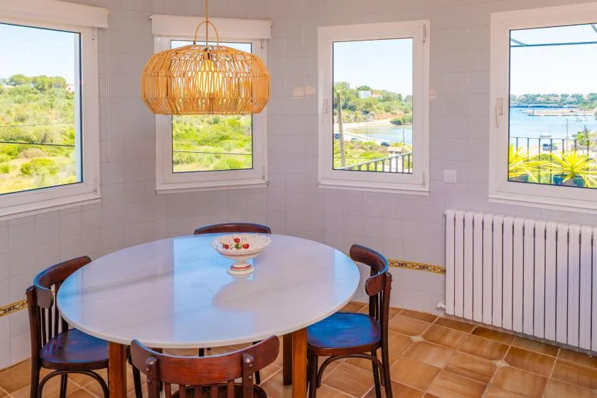 Un comedor luminoso tiene una mesa redonda bajo una lámpara colgante tejida.