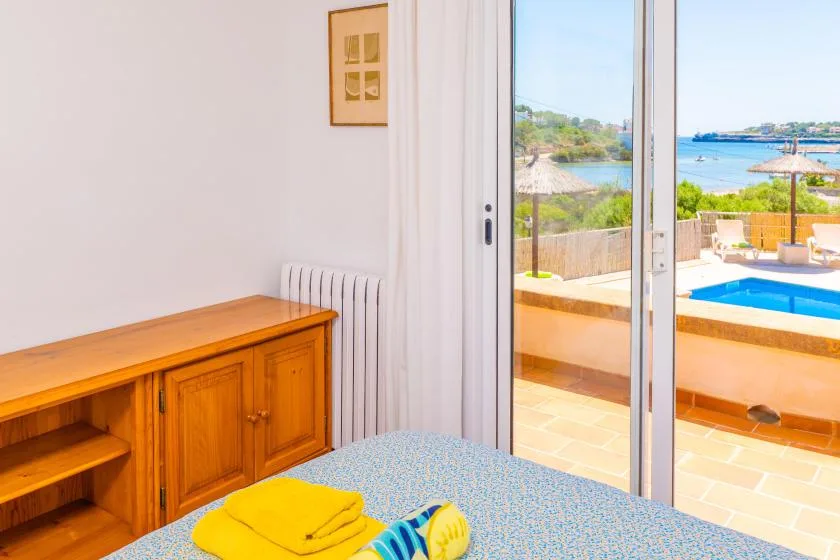 Un dormitorio con una cama junto a puertas corredizas abiertas, con vistas a una piscina y al mar.