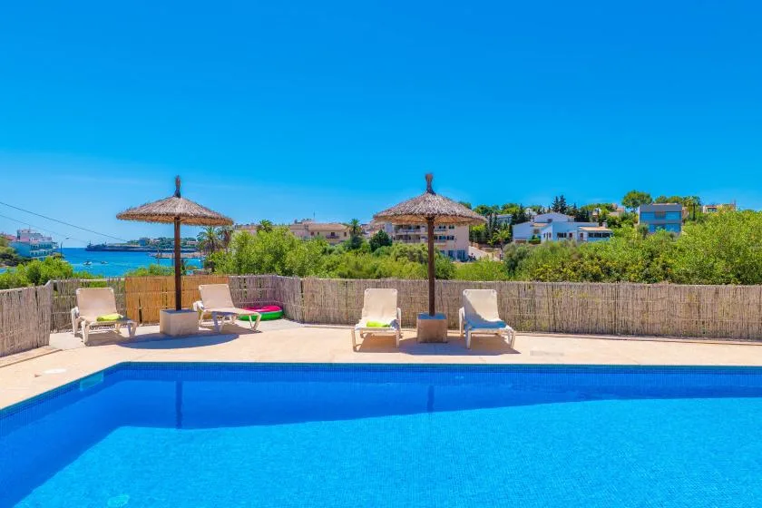 Una piscina con asientos reclinables y sombrillas junto a un muro bajo.